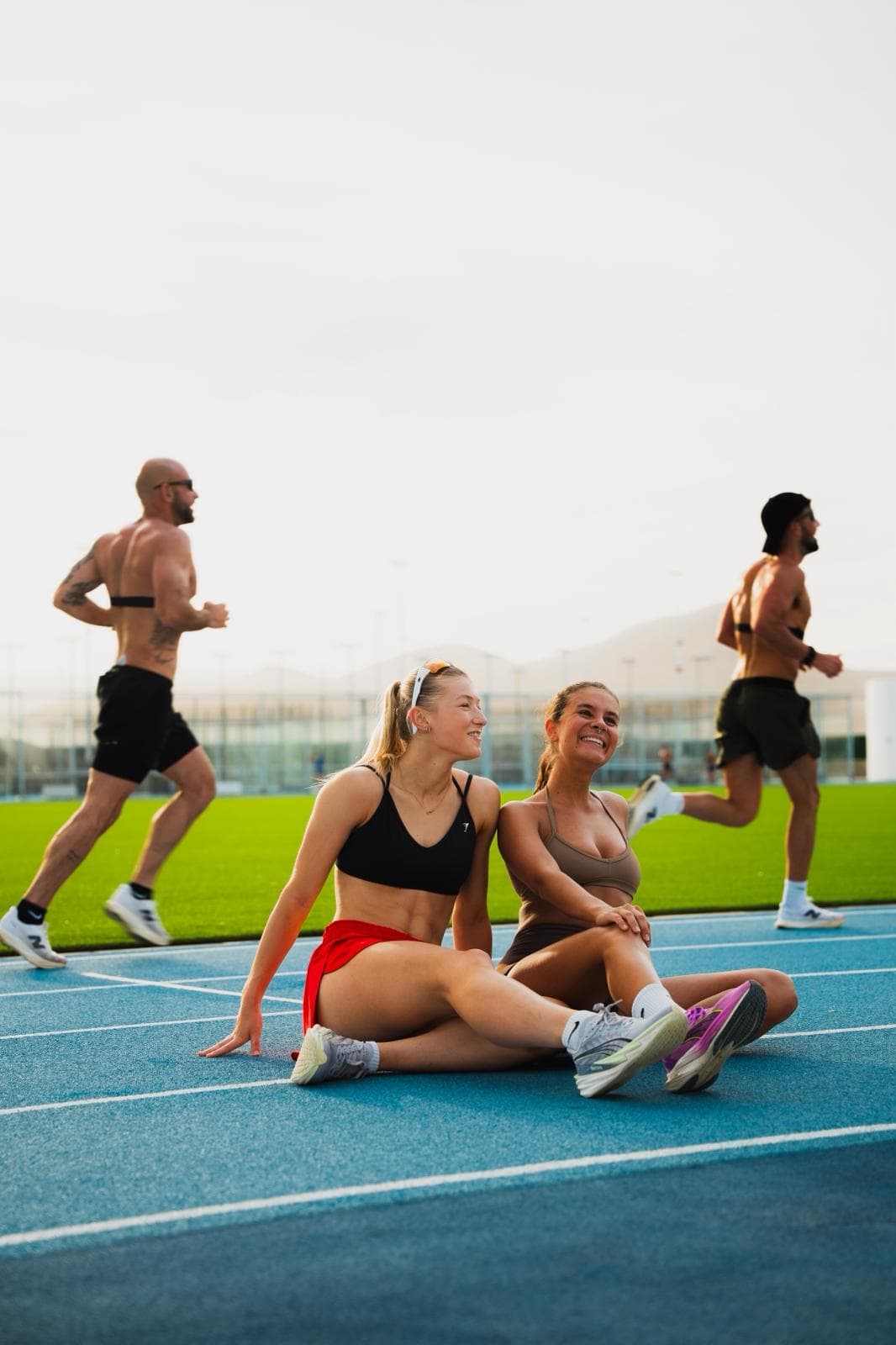 Friends resting on the track while others train behind them
